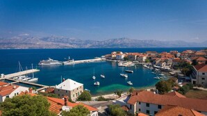 A coastal town with a marina, buildings with red-tiled roofs, and a clear view of the sea and distant mountains. - Apartment Pavlo (Postira)
