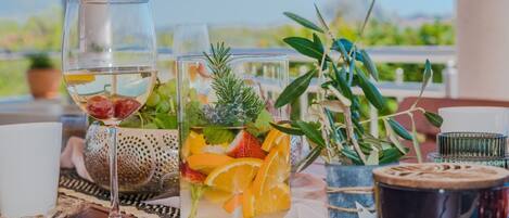 A table with a glass of white wine, a glass of water, and a glass of fruit-infused water. There are also two small potted plants and a decorative item on the table.