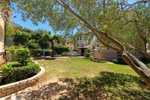 A courtyard with a stone wall, a small fountain, and surrounding greenery. - Apartments Lea (Kolan)