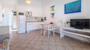 Uma cozinha moderna com armários brancos, um espaço de refeições com mesa e cadeiras, uma TV sobre um móvel e obras de arte nas paredes.