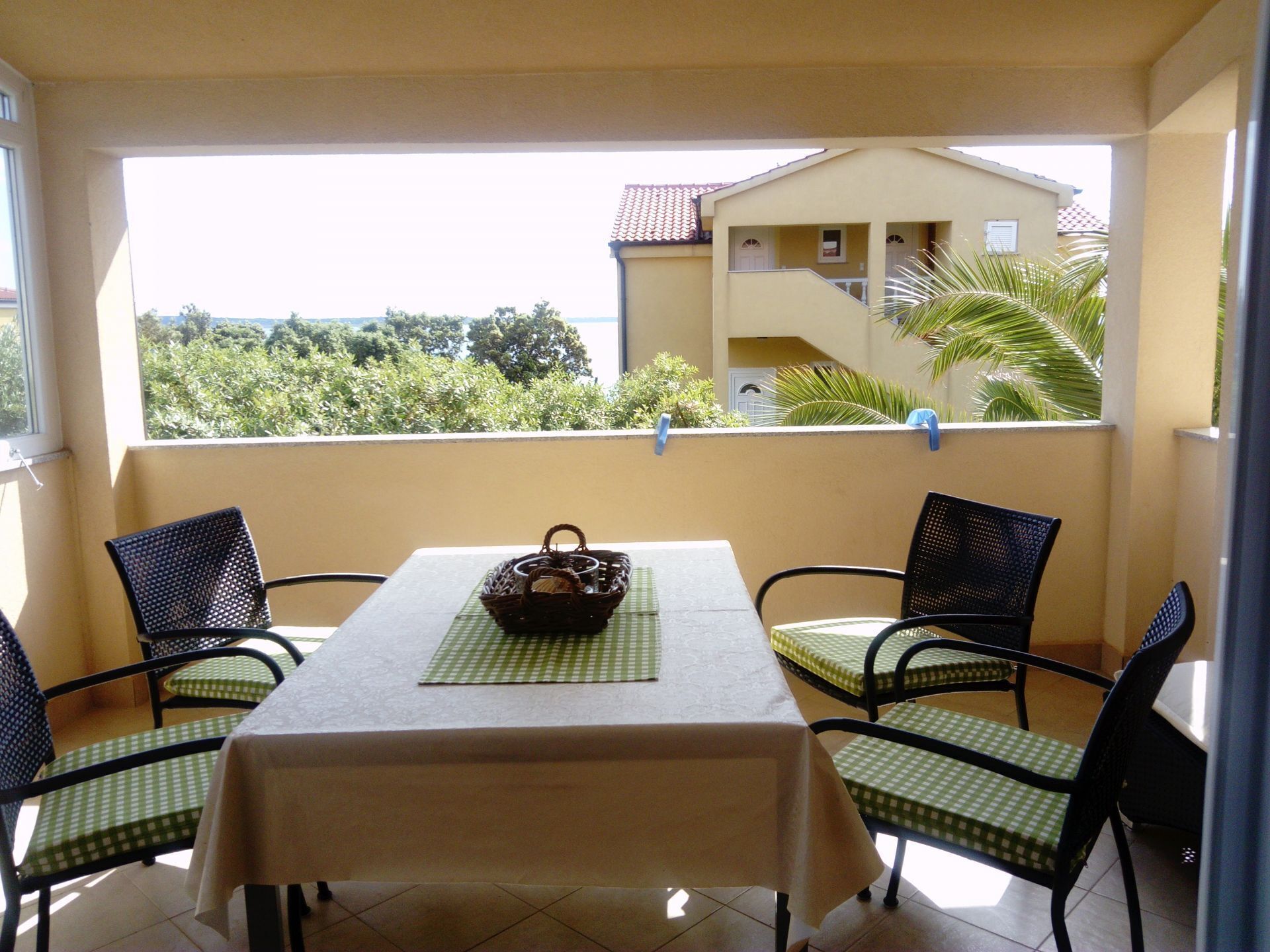 A balcony with a table and chairs, a basket, and a view of a building and trees.