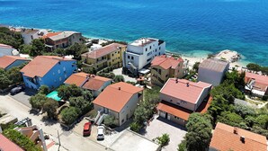 Vista aérea de uma área residencial costeira com edifícios, mar azul-claro e uma praia arenosa.