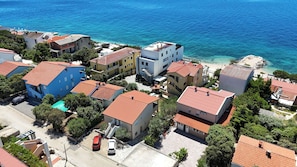 Vista aérea de uma área residencial costeira com edifícios, mar azul-claro e uma praia arenosa.
