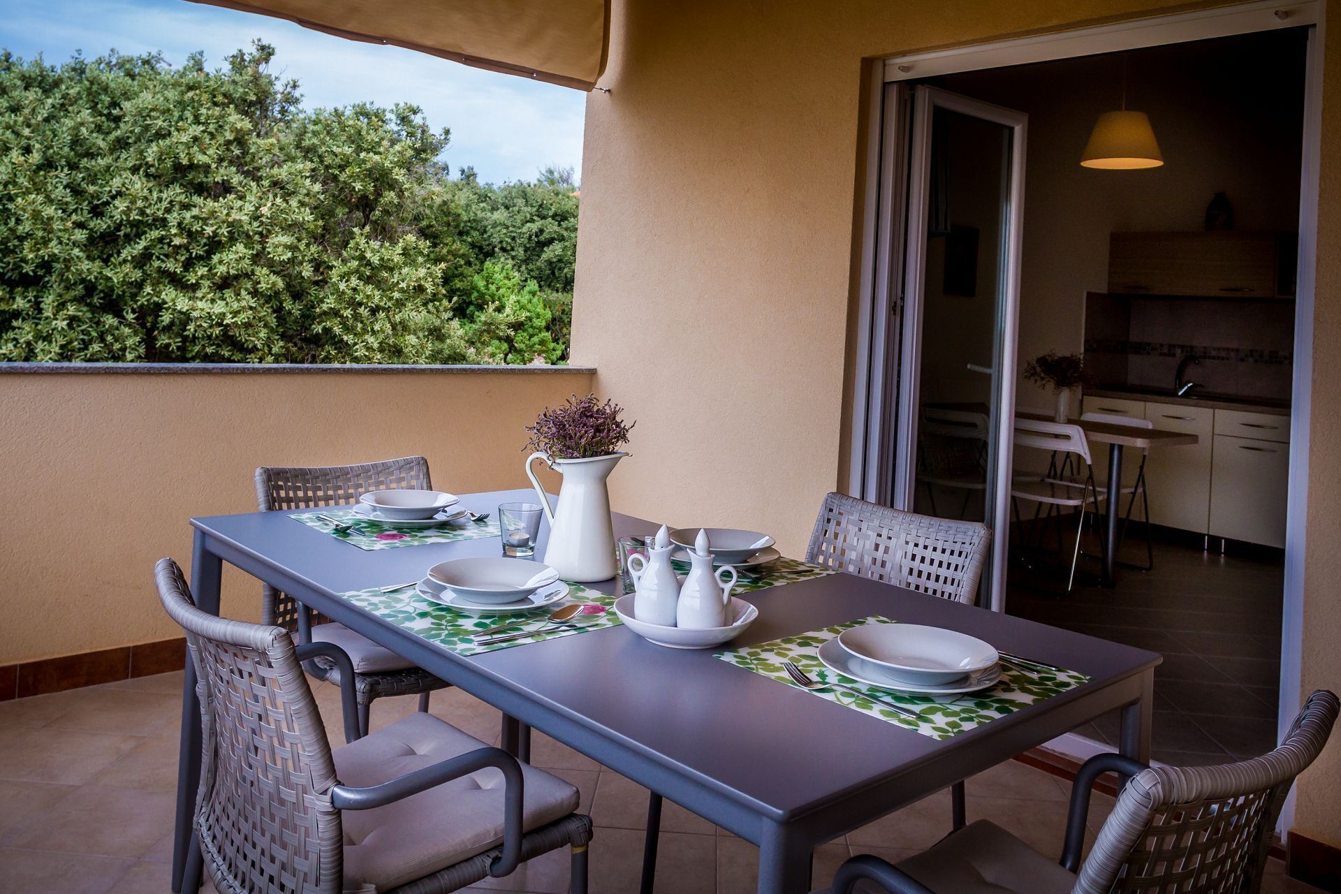 A dining table set with plates, a pitcher, and a vase on a balcony with chairs.