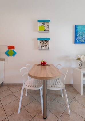 A dining area with a wooden table, white chairs, and a bowl of popcorn. - Apartments Lea (Kolan)