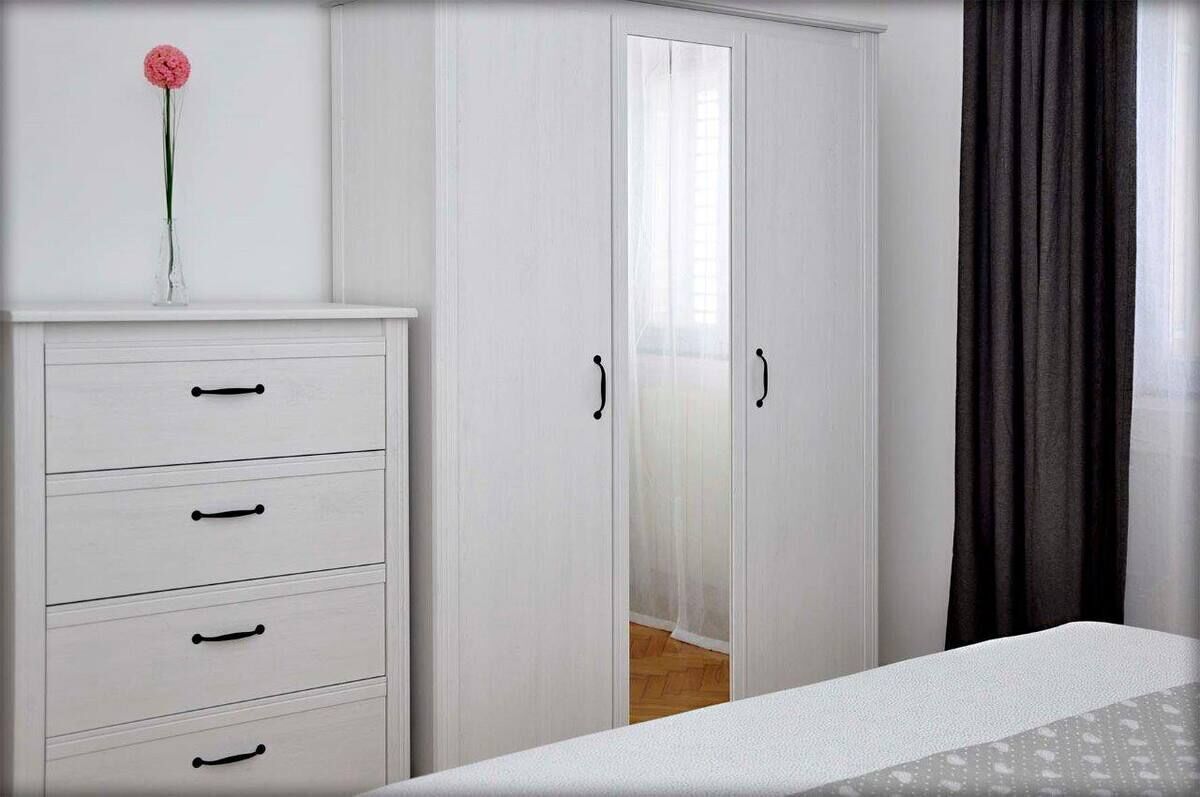 Un dormitorio con un armario blanco, una cama y una puerta con espejo.