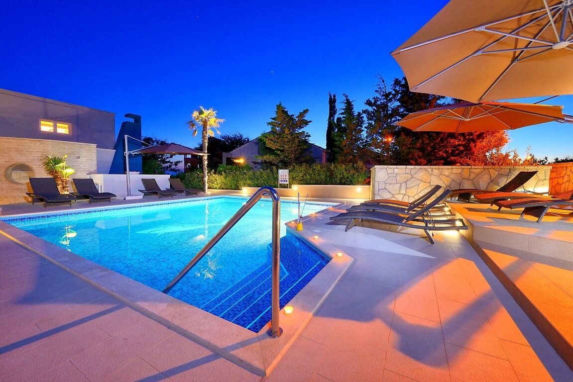 A swimming pool with lounge chairs and umbrellas, surrounded by stone walls and trees.