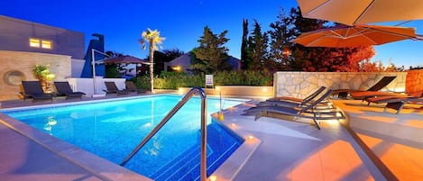 A swimming pool with lounge chairs and umbrellas, surrounded by stone walls and trees.