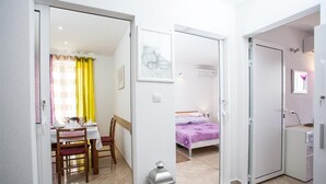 Quarto de hotel moderno com área de refeições, cama com colcha roxa e armário branco.