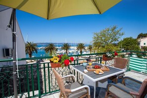 A balcony with a table set for breakfast, overlooking a marina with boats and a clear blue sky. - Apartment Rilka (Baska Voda)
