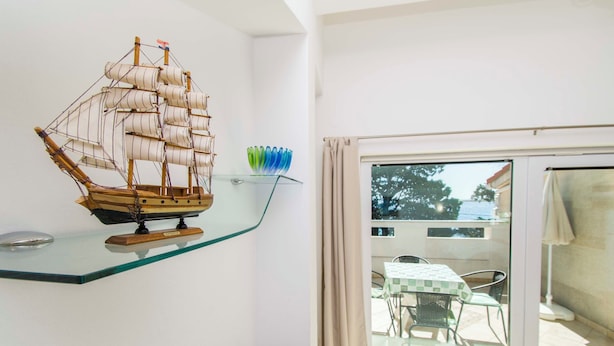 A model ship on a glass shelf, a patterned cushion, and a view of an outdoor patio with a table and chairs. - Apartment Gordana (Pag)