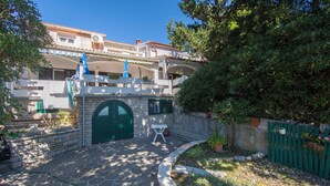 A courtyard with a stone pathway, a green door, and a white table. - Apartment Gordana (Pag)