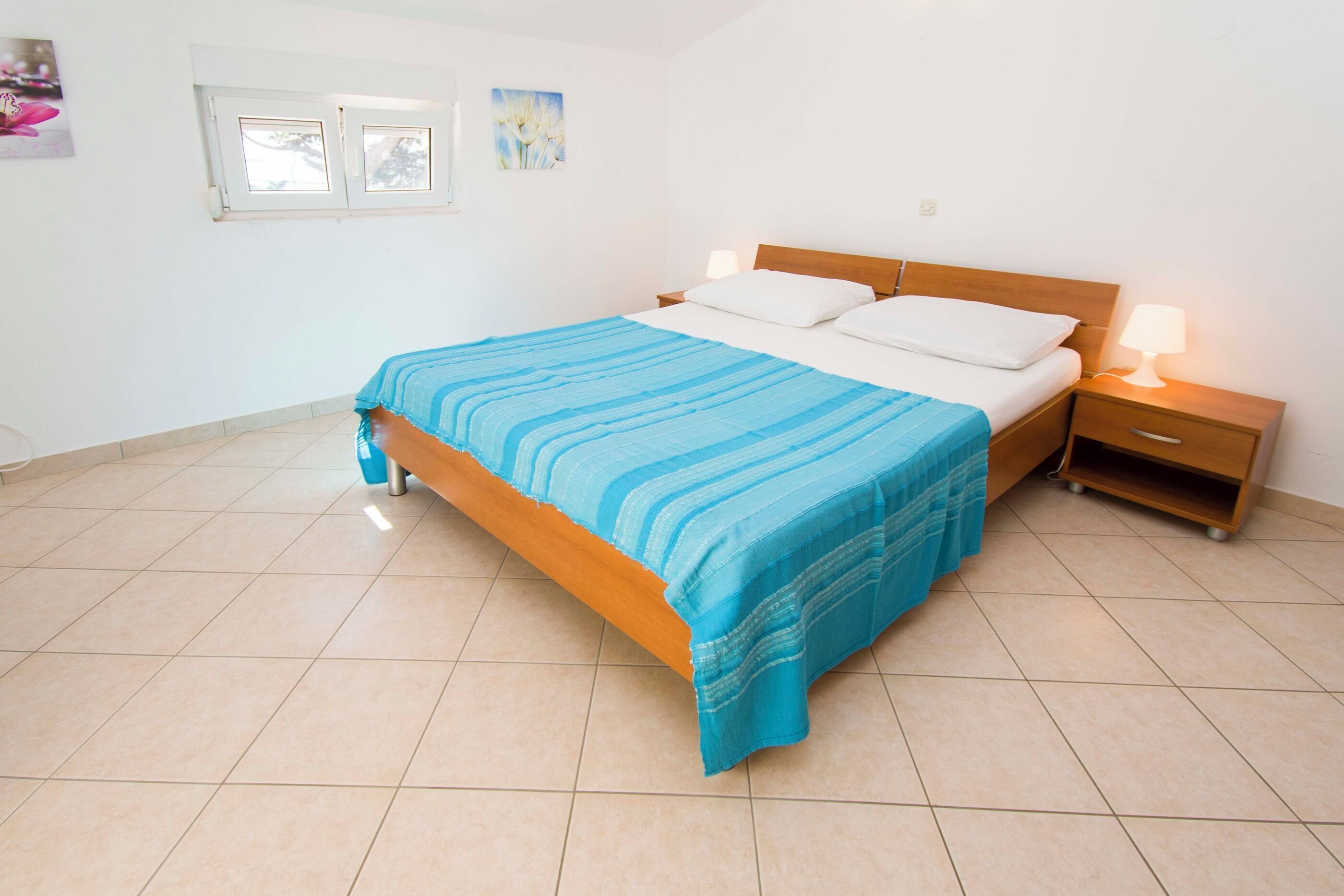 A bedroom with a bed, nightstands, a window, and a wall-mounted picture.