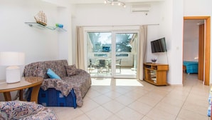 A living room with a sofa, a small table, a TV, and a sliding glass door leading to an outdoor area. - Apartment Gordana (Pag)