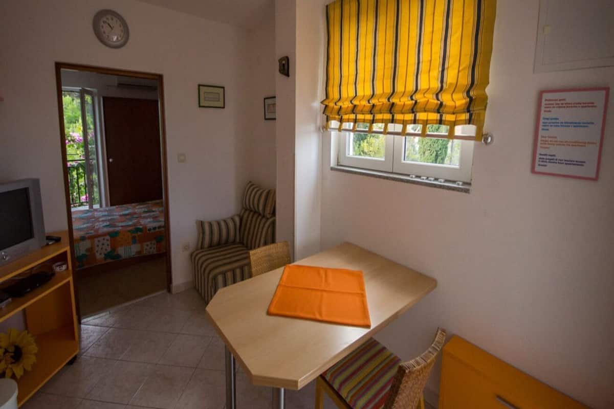 A small room with a table, a chair, a television, and a window with yellow curtains.
