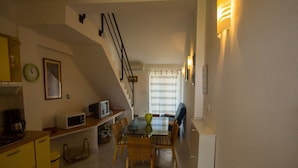A compact kitchen with yellow cabinets, a dining table with chairs, a microwave, and a clock on the wall. - Apartments Daju (Pasman)