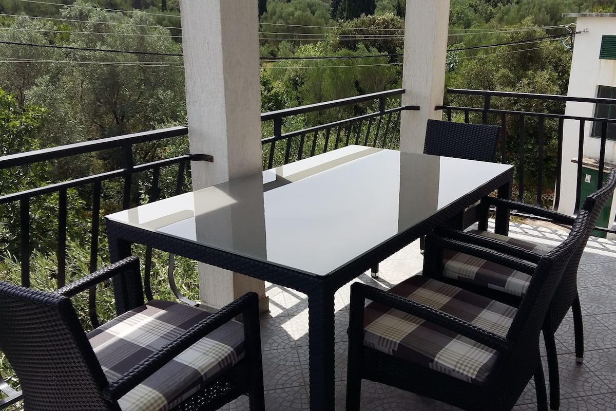 A balcony with a glass table and wicker chairs, surrounded by a metal railing.