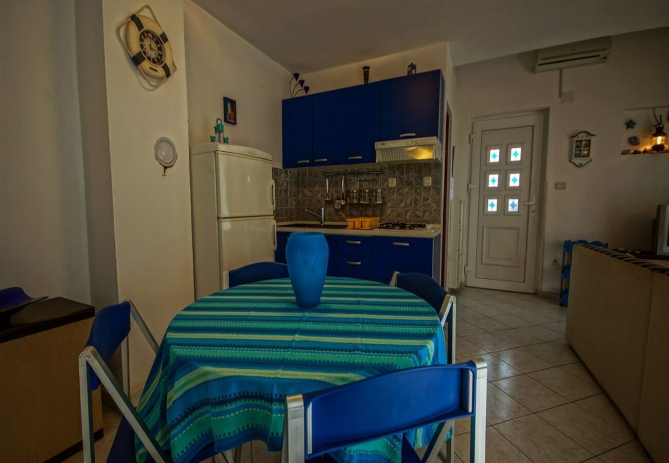 Une cuisine de taille réduite avec des meubles bleus, un réfrigérateur blanc et un coin repas comprenant une table et des chaises bleues.