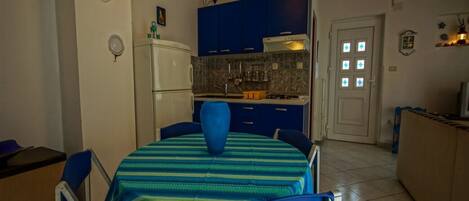 Une cuisine de taille réduite avec des meubles bleus, un réfrigérateur blanc et un coin repas comprenant une table et des chaises bleues.