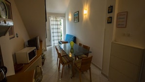 A dining area with a glass table, wooden chairs, a blue sofa, and a microwave on the counter. - Apartments Daju (Pasman)
