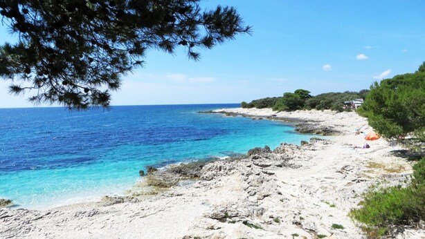 A rocky beach with clear blue water, a few people, and some greenery. - Apartments Oasis (Sali)