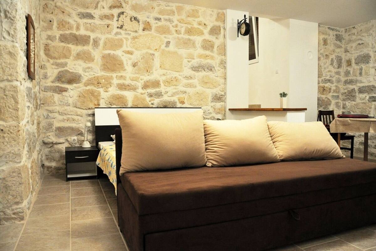 Une pièce chaleureuse avec un mur en pierre, un canapé marron agrémenté de coussins beige, une table de chevet et un petit bureau avec une chaise.