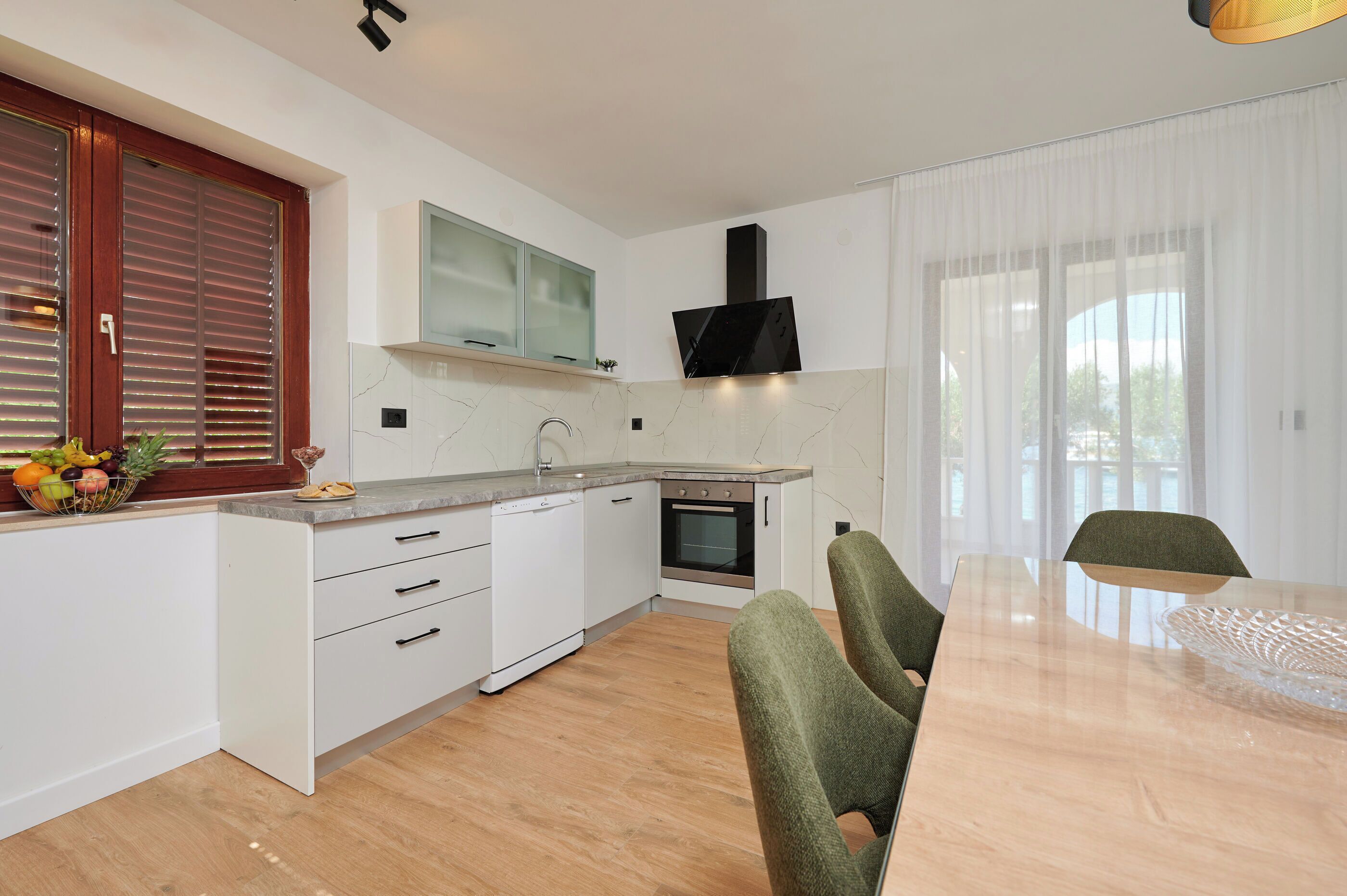 Una cocina moderna con armarios blancos, horno integrado y zona de comedor con mesa y sillas.