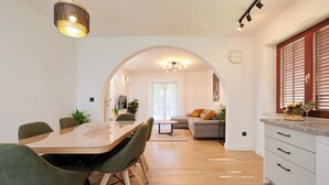 A modern kitchen with a dining area, featuring a wooden table, green chairs, and a built-in oven. - Apartment Natali (Okrug)