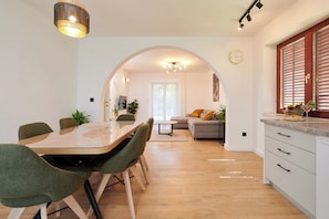 A modern kitchen with a dining area, featuring a wooden table, green chairs, and a built-in oven. - Apartment Natali (Okrug)