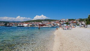 A beach with clear shallow water, a pebble beach, and a town in the background. - Apartment Natali (Okrug)