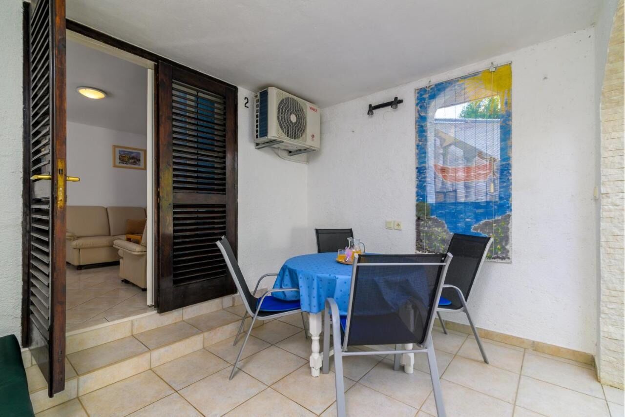 A small dining area with a table and chairs, an air conditioning unit, and a view of a building through a window.