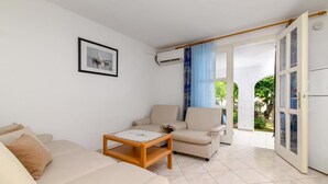 Un salon comprenant un canapé, un fauteuil, une table basse et une porte donnant sur un balcon.
