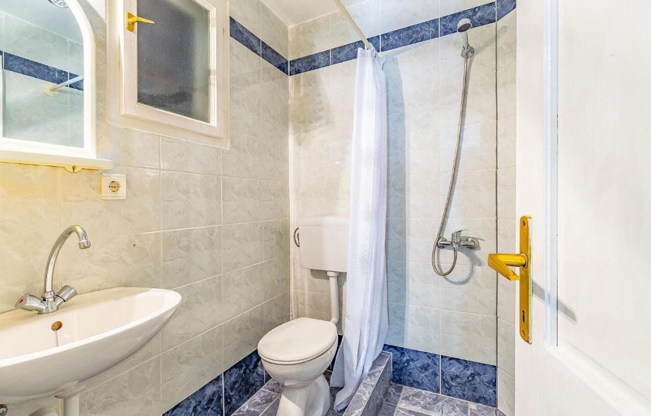 A bathroom with a sink, toilet, shower, and a window.