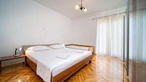 A bedroom with a wooden bed, a nightstand with a lamp, and a window with curtains. - Apartments Bepa (Lopar)