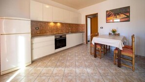 A compact kitchen with white cabinets, a built-in oven, and a dining area with a table and chairs. - Apartments Bepa (Lopar)