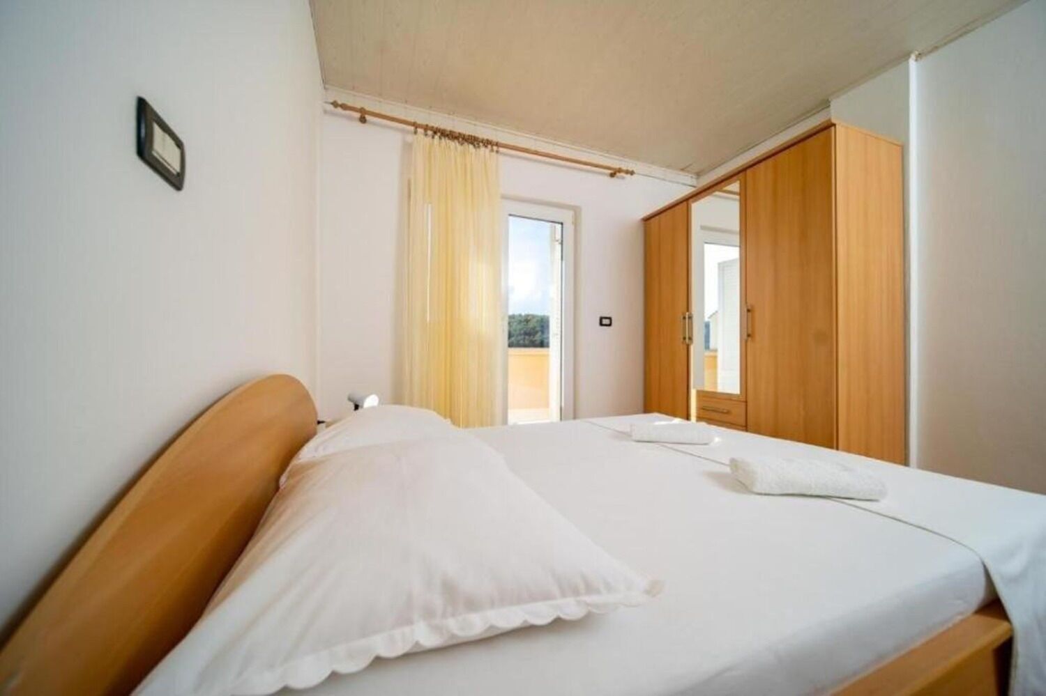 Een slaapkamer met een houten bed, witte beddengoed, een spiegel en een kledingkast.