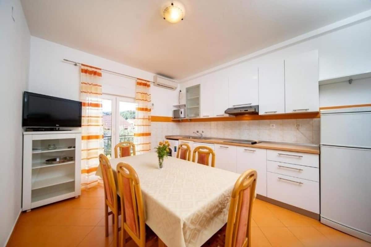 A compact kitchen with white cabinets, a microwave, and a TV on a shelf.