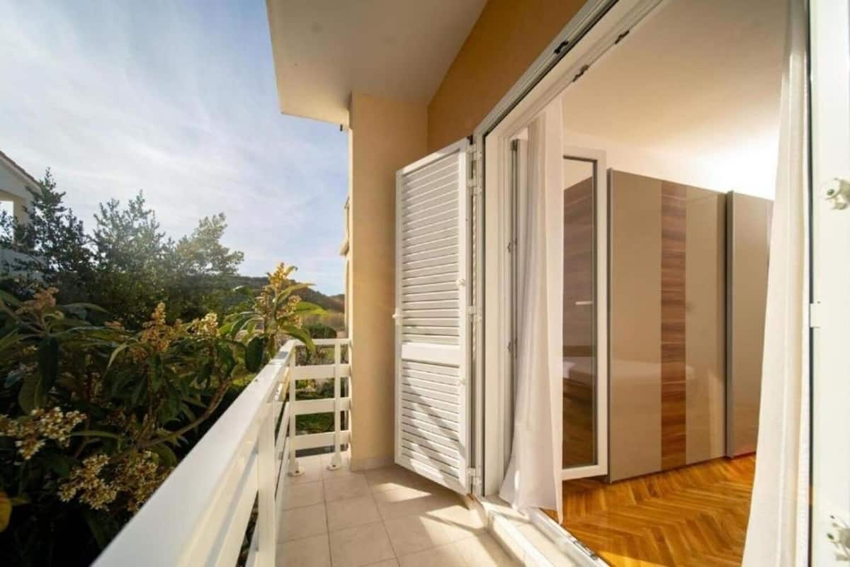 A balcony with a white railing, a sliding glass door, and a view of greenery and hills.