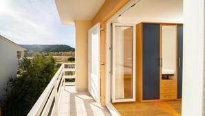 A balcony with a view of a hilly landscape, a sliding glass door, and a wooden cabinet. - Apartments Bepa (Lopar)