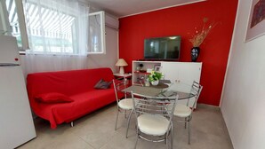 A compact living space with a red sofa, a small dining table with chairs, a TV mounted on the wall, and a refrigerator. - House Vlasta (Primosten)