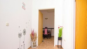 A hallway with a dining area in the background, a white wall with a dandelion decoration, a potted plant, and a door. - Apartment Tina (Obrovac)