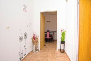 A hallway with a dining area in the background, a white wall with a dandelion decoration, a potted plant, and a door. - Apartment Tina (Obrovac)