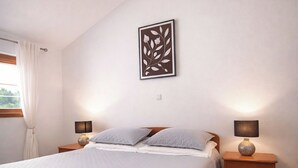 A bedroom with a bed, two bedside tables, a wall-mounted artwork, a window with curtains, and a rug. - Apartment Tina (Obrovac)