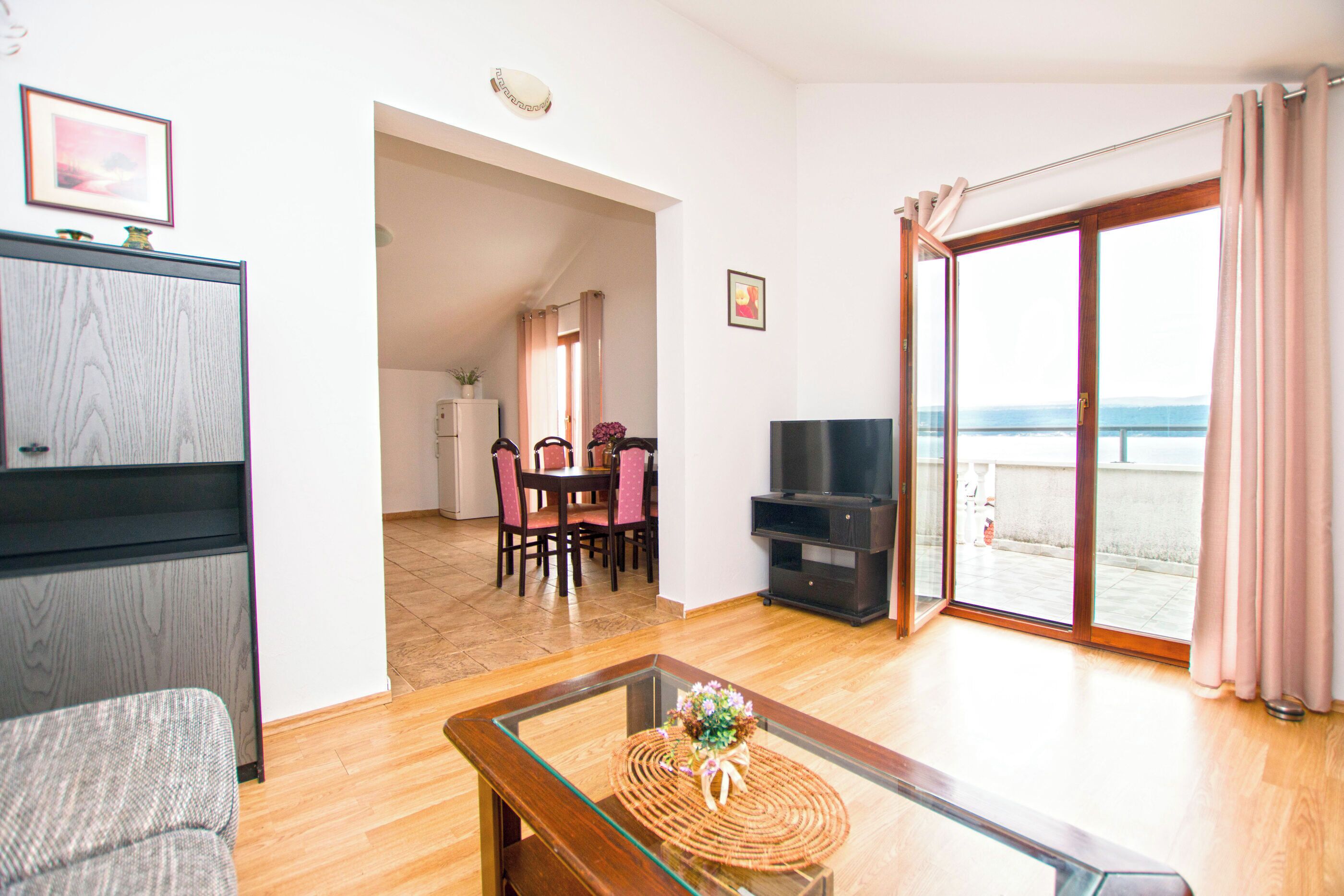 Sala de estar com sofá, mesa de centro de vidro, televisão e área de jantar com cadeiras e mesa.