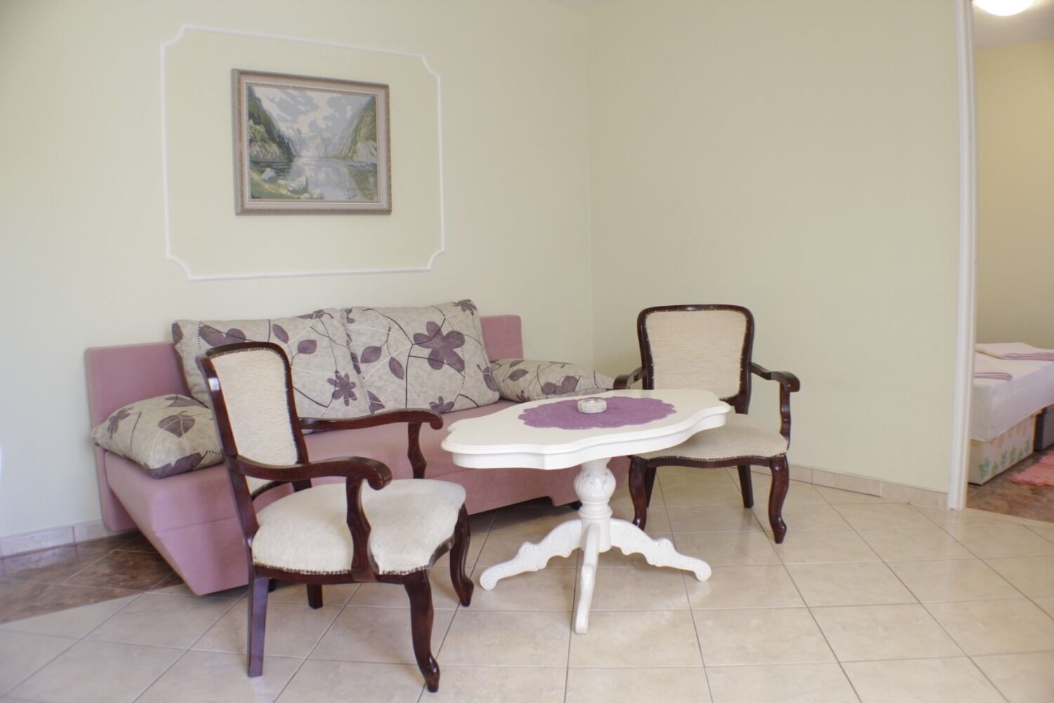 A living room with a sofa, two armchairs, a small round table, and a framed painting on the wall.