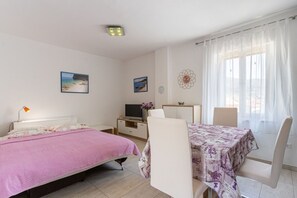 A bedroom with a bed, a desk, a chair, a TV, and a window with curtains. - Apartment Mici 2 (Cres)