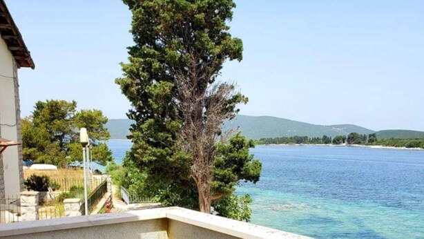 A balcony with a table and two chairs, overlooking a body of water and a tree. - Apartment Blue (Mali Losinj)