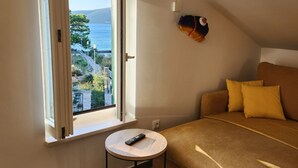 A bedroom with a bed, a round table with a remote, and a window with an open view of a landscape. - Apartment Blue (Mali Losinj)
