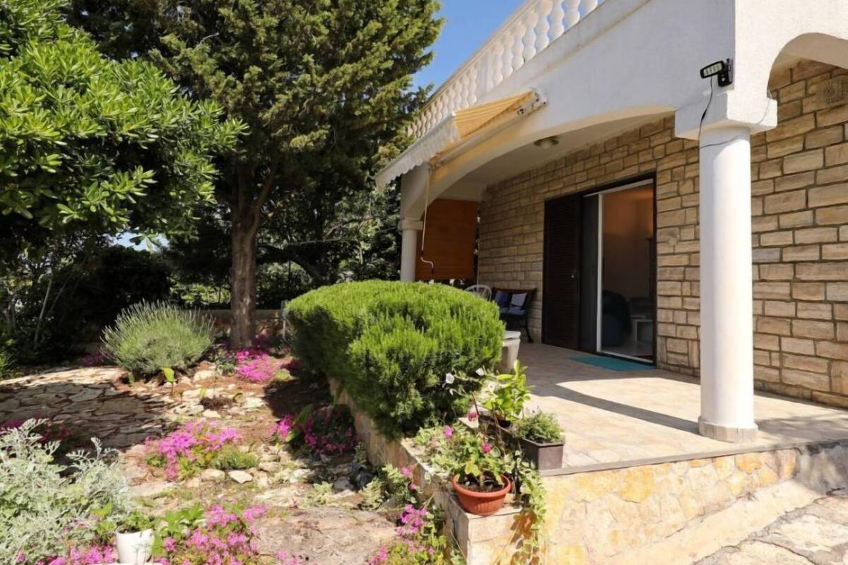 A house with a stone facade, a covered porch, and a garden with various plants and flowers.