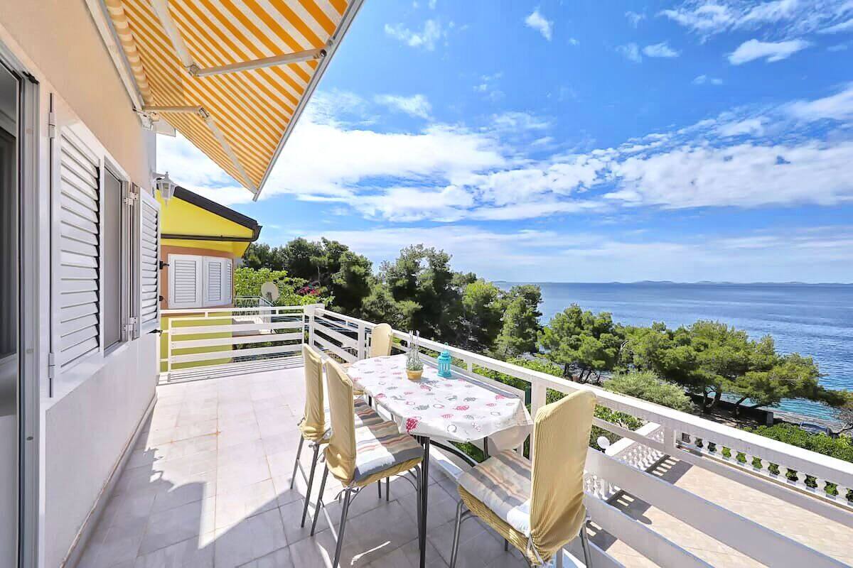 A balcony with a table and chairs, overlooking a body of water and greenery.